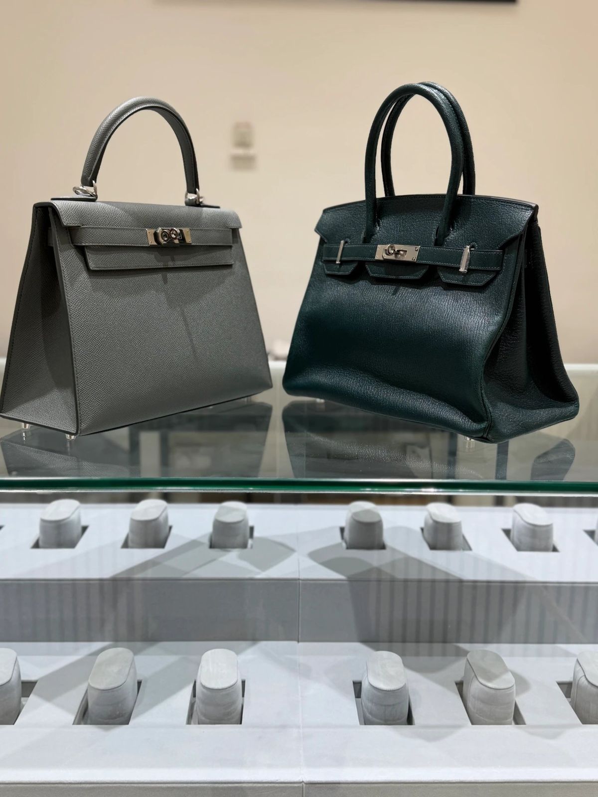 Hermès Kelly and Birkin displayed side by side in a showroom cabinet