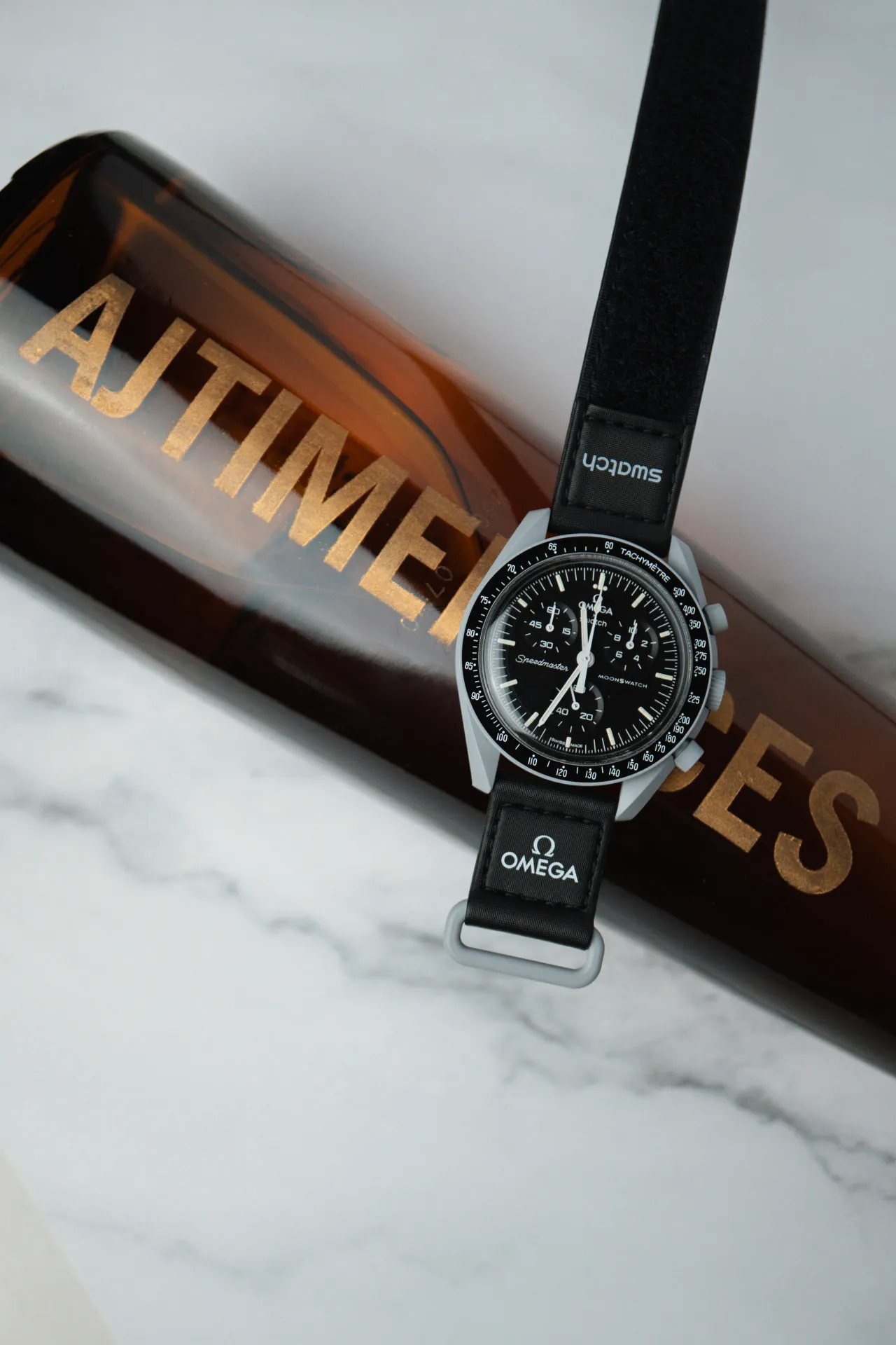 Omega x Swatch MoonSwatch Speedmaster resting on an AJ Timepieces bottle