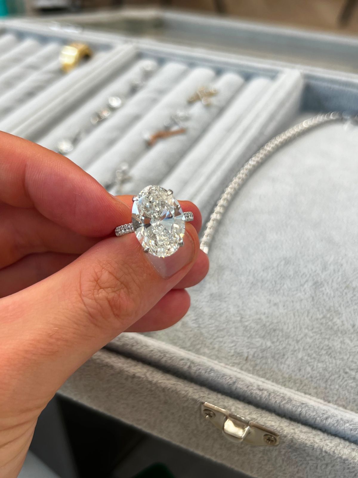 Oval cut diamond solitaire with a pave band held above a jewellery tray